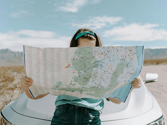 Women holding a map learning against a car in the desert