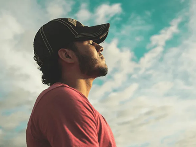 man taking a deep breath in reflection with clouds in the background