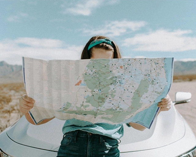 Women holding a map learning against a car in the desert