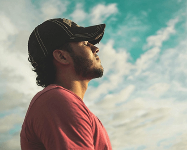 man taking a deep breath in reflection with clouds in the background